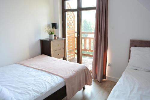 a bedroom with two beds and a window with a balcony at Apartamenty Wilcza Knieja in Zawóz