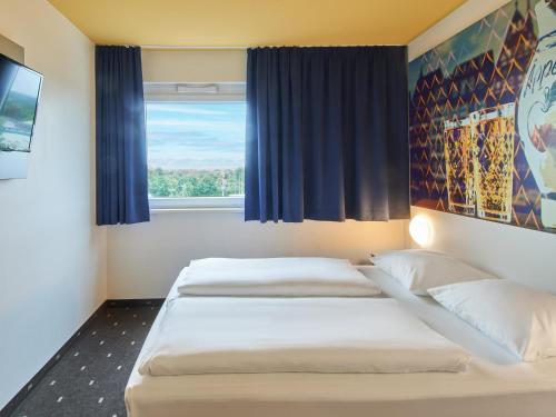 2 Betten in einem Zimmer mit Fenster in der Unterkunft B&B Hotel Frankfurt-Nord in Frankfurt am Main