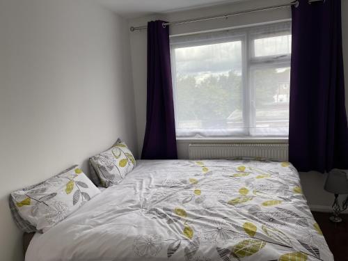 a bed in a room with a window and a bedspread at Immaculate 4-Bed House near Heathrow airport in Hayes