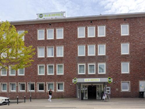 duży budynek z czerwonej cegły z kobietą stojącą na zewnątrz w obiekcie B&B Hotel Duisburg Hbf-Nord w mieście Duisburg