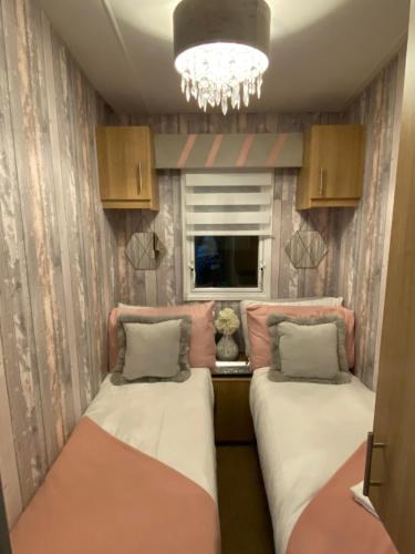 two beds in a room with a window and a chandelier at Sandylands Holiday Home in Stevenston