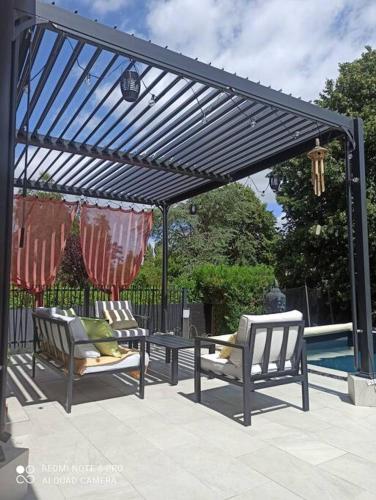 a pergola with two chairs and a table next to a pool at Charmante maison avec piscine chauffée, salle de cinéma et bar in Auffargis
