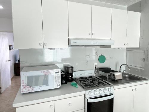 a white kitchen with a stove and a microwave at Brisas Shores 07 Beachfront Condo, Pool and garden area, Zona Hotelera Cancun in Cancún