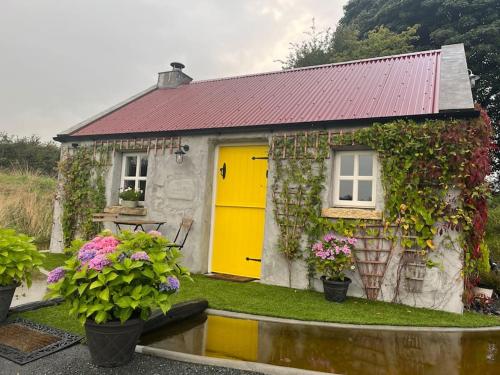 a small house with a yellow door and flowers at The Nest Quaint Luxury Cottage Getaway in Tiragarvan