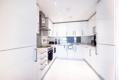 a white kitchen with white cabinets and a sink at Modern 12th Floor | Balcony Striking London View in London