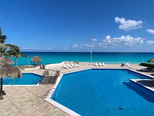 a swimming pool with the ocean in the background at Brisas Shores 07 Beachfront Condo, Pool and garden area, Zona Hotelera Cancun in Cancún