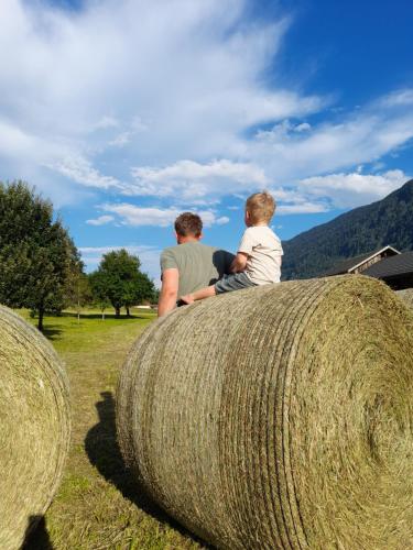a man and a boy sitting on top of a large roll of hay at Rauterhof in Hermagor