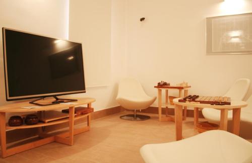 a living room with a flat screen tv and white chairs at Mediterraneo Guesthouse in Giardini Naxos
