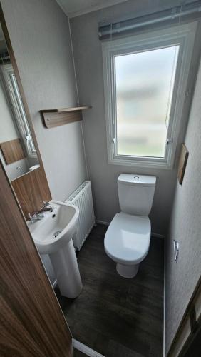 a bathroom with a toilet and a sink and a window at Haven Kent Coast Allhallows sleeps 8 in Allhallows