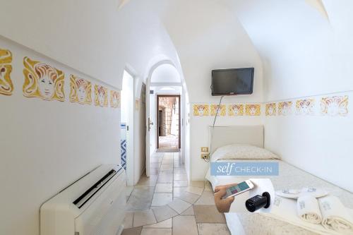 Dimora Dell'Osanna Raro Villas Smart Rooms Collection في كاروفينيو: غرفة بيضاء مع سرير وتلفزيون على الحائط