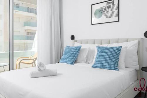 un letto bianco con cuscini blu in una camera da letto di דירה משפחתית מפנקת 50 מטר מהים - By Edom a Eilat