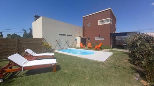 een achtertuin met een zwembad en stoelen en een huis bij EL BAGUAL DE MONTE in San Miguel del Monte
