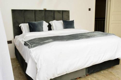 1 cama grande con sábanas y almohadas blancas en The White House, en Eldoret