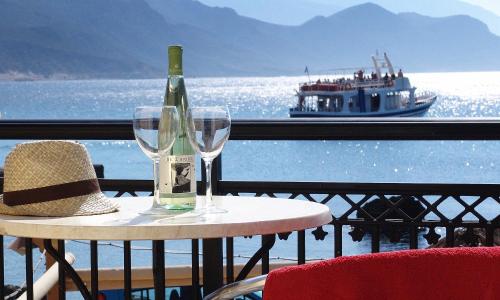 a bottle of wine and two glasses on a table with a boat at Harbour Studios And Apartments in Palaiochóra