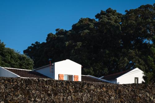 uma casa branca atrás de uma parede de pedra com árvores ao fundo em ENTRE MUROS - Turismo Rural - Casa com jardim e acesso direto ao mar em Ribeira Grande