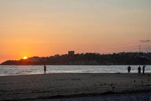 a group of people standing on the beach at sunset at Casa Daikiri in Puerto Escondido