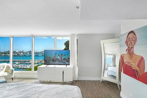 a white bedroom with a television and a large window at The Palms! Direct water view corner condo in Miami