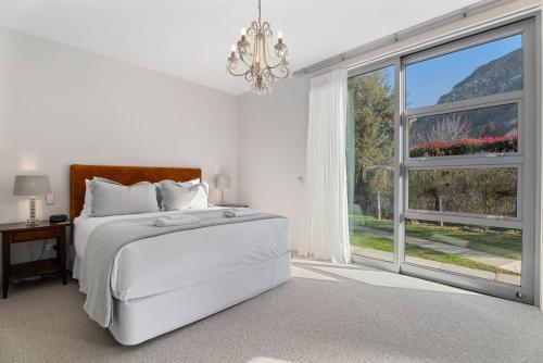 a white bedroom with a bed and a large window at Kinsale - Spa, Pool, Gym and Tennis! in Arrowtown