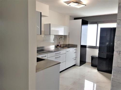 La cuisine est équipée de placards blancs et d'un réfrigérateur noir. dans l'établissement 4bdrm - 110mr - Dream vacation apartment, à Tibériade