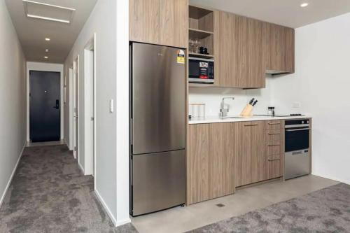 Hagley Park Apartment في كرايستشيرش: مطبخ مع ثلاجة ستيل ستانلس ودواليب خشبية