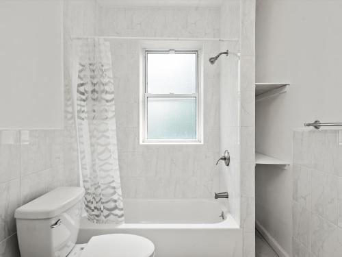 een witte badkamer met een toilet en een raam bij Oakland/University @C Modern & Stylish Private Bedroom with Shared Bathroom in Pittsburgh
