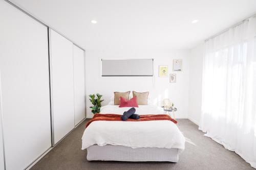 a white bedroom with a large bed with red pillows at Cozy Home Close to Beach and Hobart CBD in Hobart