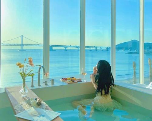 una mujer sentada en una bañera con vistas a un puente en Stay moment, en Busan