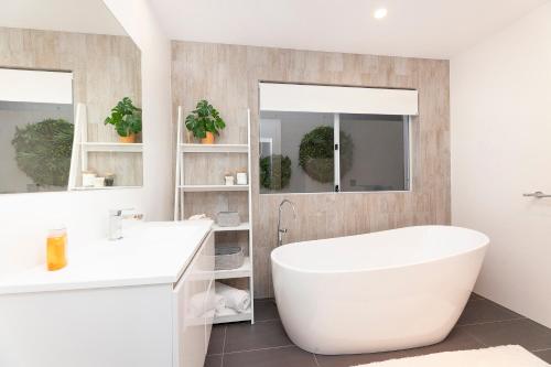 La salle de bains blanche est pourvue d'une baignoire et de deux lavabos. dans l'établissement Palm Breeze, à Forster