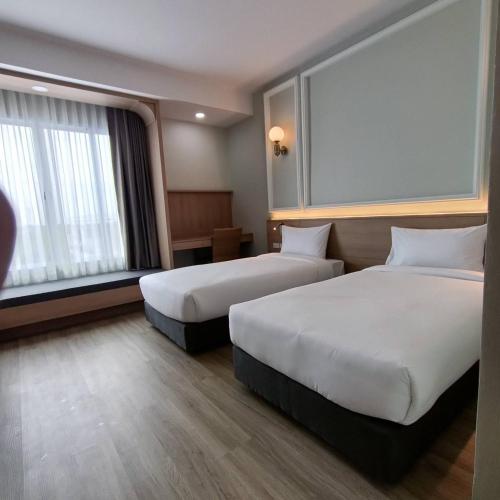 a hotel room with two beds and a window at Mayflower Grande Suite Hotel in Phitsanulok