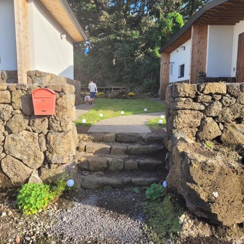 a stone retaining wall with a stone staircase in a yard at Joohane Jejudo House in Jeju