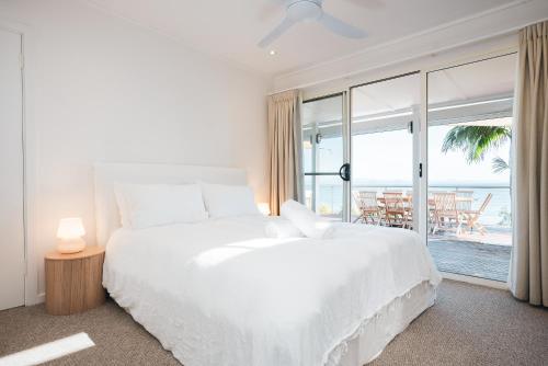 a white bedroom with a large bed and a large window at Wategos Villa in Byron Bay