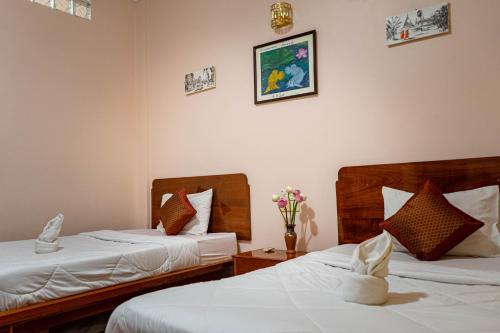 Nawin Palace Guesthouse في بنوم بنه: سريرين في غرفة الفندق مع ورود على الحائط