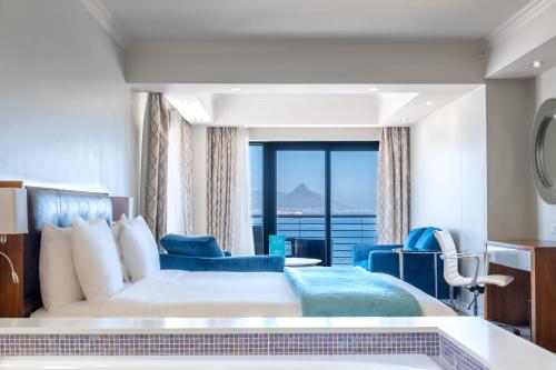 a hotel room with a bed and a large window at Blaauwberg Beach Hotel in Bloubergstrand