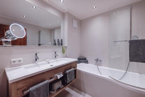 a bathroom with a sink and a tub and a mirror at Familienresort Ellmauhof - das echte All Inclusive in Saalbach Hinterglemm