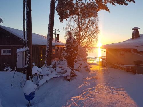 a snow covered yard with a house with the sun setting at Trevligt gästhus nära Vänern och badplats in Hammarö
