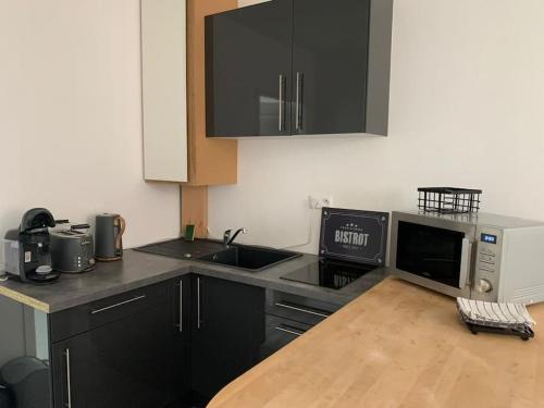 La cuisine est équipée de placards noirs, d'un évier et d'un four micro-ondes. dans l'établissement Studio en centre ville d'Argentan, à Argentan