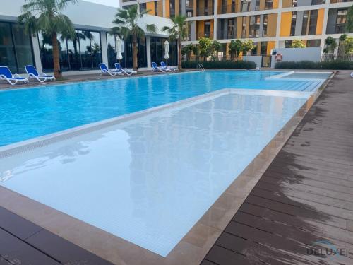 a large swimming pool with blue chairs and a building at Classic Studio at Mesk 1 Midtown Dubai Production City by Deluxe Holiday Homes in Dubai