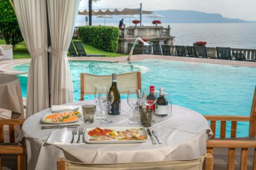 a table with plates of food and wine on it next to a pool at Hotel Villa Capri in Gardone Riviera