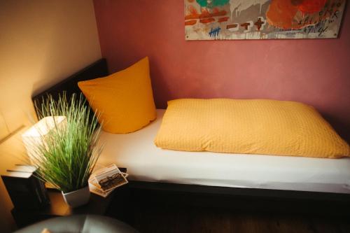 Bett mit gelbem Kissen und Topfpflanze in der Unterkunft Stadthotel Kleiner Berg in Friedrichshafen