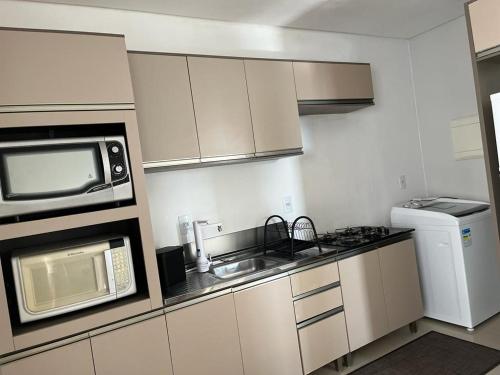 a small kitchen with a microwave and a sink at Apartamento à 400m do mar in Itapema