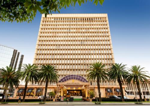 un grand bâtiment avec des palmiers devant lui dans l'établissement Duxton Hotel Perth, à Perth