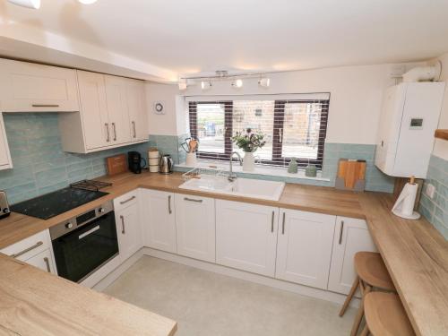 a kitchen with white cabinets and a sink at Smithy Cottage in Dronfield