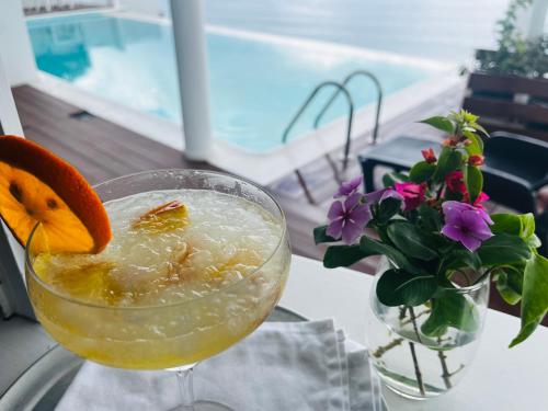 a drink with an orange on a table with a vase of flowers at Fogo Boutique Hotel in São Filipe