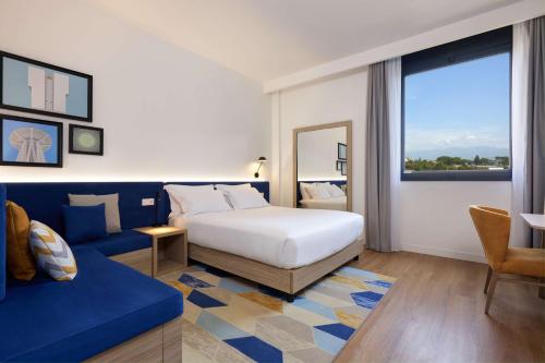 Habitación de hotel con cama y sofá azul en Hampton by Hilton Rome North Fiano Romano, en Fiano Romano