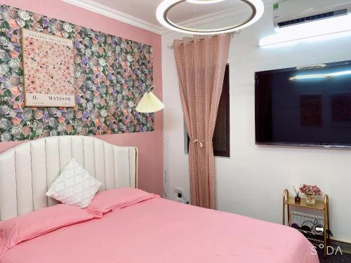 um quarto com uma cama rosa e uma televisão de ecrã plano em FlowerGod Apartments - BlackPink HomeStay em Hanói