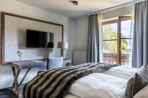 a hotel room with a bed and a desk and a window at Alpenhof Murnau in Murnau am Staffelsee