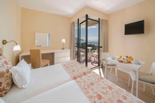 フンシャルにあるDorisol Mimosa Studio Hotelのベッド、テーブル、バルコニーが備わる客室です。