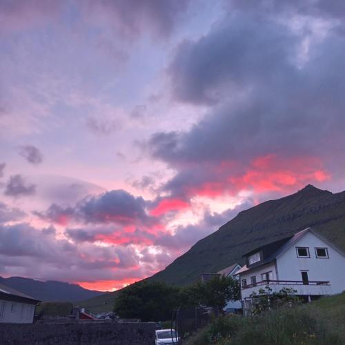 a sunset in the mountains with a white house at Experience unique Faroe Islands holiday home by the sea with great views, fully equipped kitchen and reliable Wi-Fi in Norðragøta