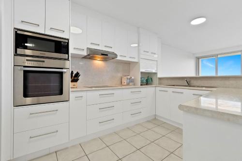 a white kitchen with white cabinets and appliances at Oceanfront apartment on top of point Cartwright in Buddina