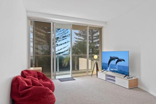 a living room with a red chair and a television at Oceanfront apartment on top of point Cartwright in Buddina